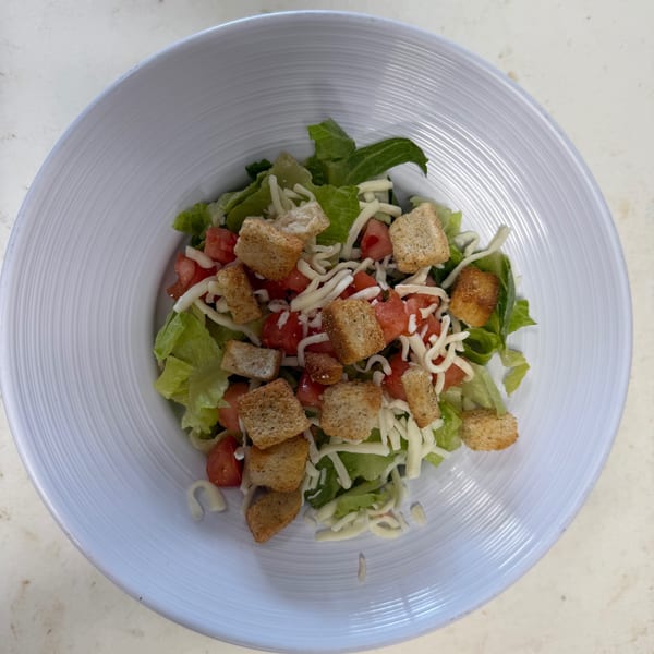 A fresh garden salad with lettuce, diced tomatoes, shredded cheese, and croutons in a white bowl.