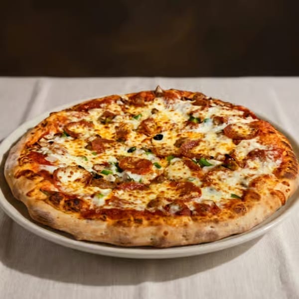 A whole pepperoni and sausage pizza with green peppers and black olives on a white plate.