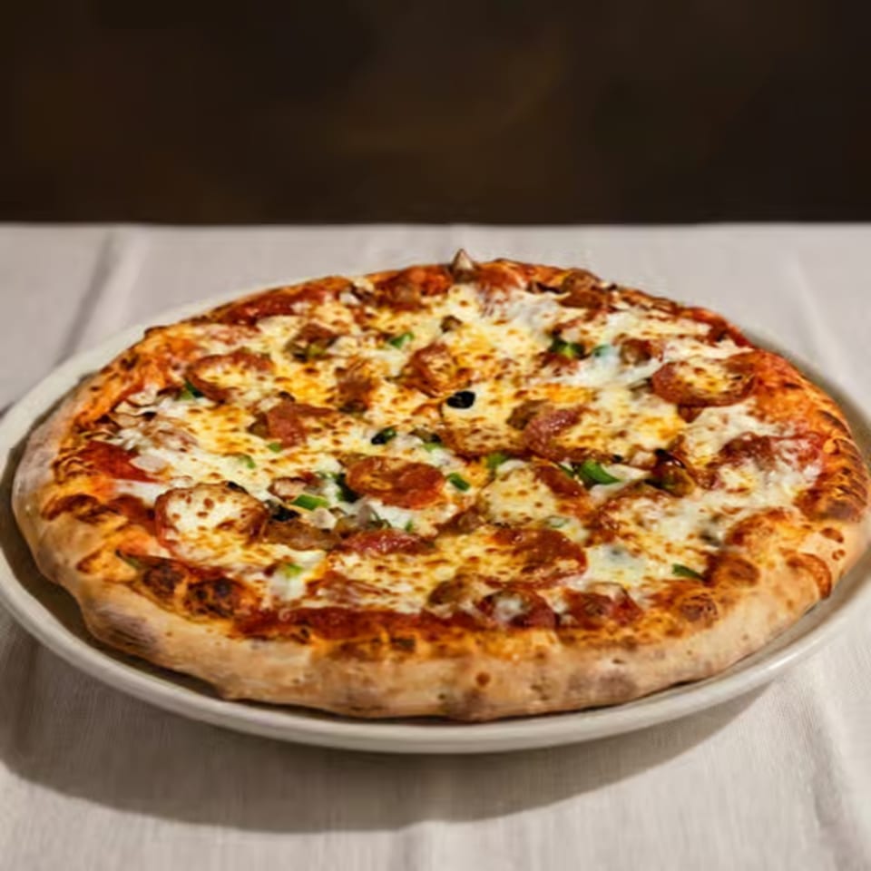 A whole pepperoni and sausage pizza with green peppers and black olives on a white plate.